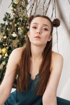 New year shooting. Beautiful young girl in lingerie smiling sitting on bed background decorated with Christmas tree and gifts in her cozy bedroom.