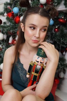 Beautiful young girl holds a wooden nutcracker toy near a decorated Christmas tree