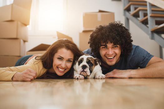 Portrait of a cheerful young couple posing with their English bulldog puppy while moving into their new home. Looking at camera.