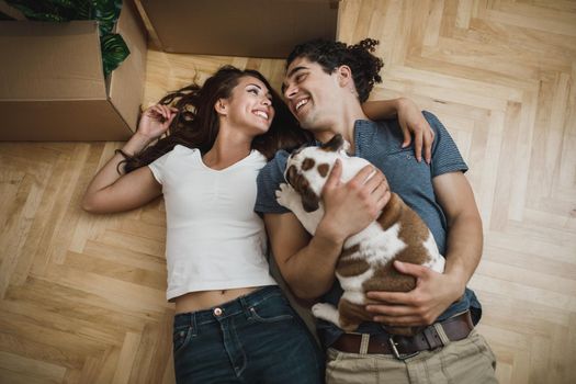 Top view of a happy young couple taking a break and having fun with their English bulldog puppy while moving into their new home.
