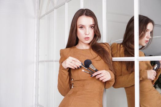 Makeup artist with long dark hair holding a powder brush, haughty expression, reflection in the mirror