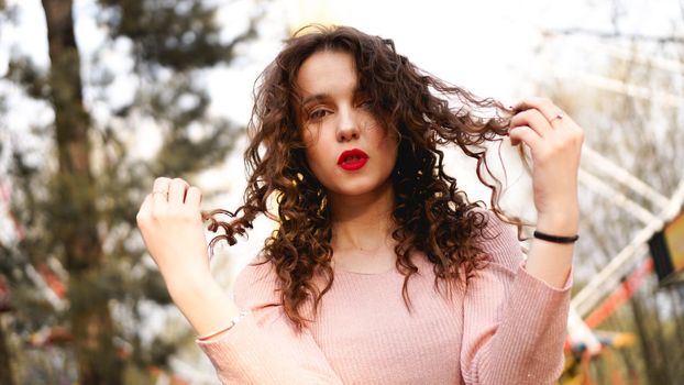 Women with long curly hair in the background of the Ferris wheel in sunny day