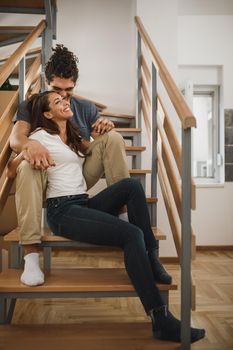 A smiling young couple in love sitting on stairs and taking a break while moving into their new home.