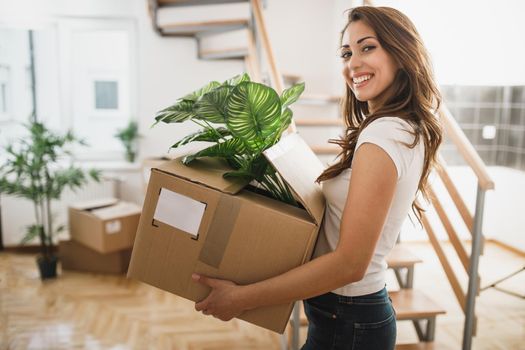Portrait of a smiling young woman carrying a cardboard box on moving into her new house.