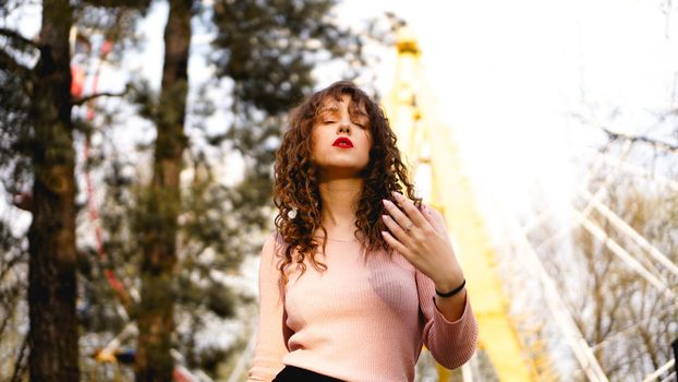 Women with long curly hair in the background of the Ferris wheel in sunny day