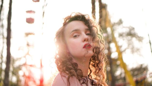 Closeup of a beautiful young woman with curly hair - a sunset behind her