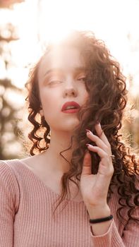 Closeup of a beautiful young woman with curly hair - a sunset behind her