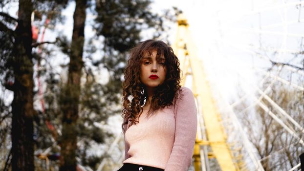 Women with long curly hair in the background of the Ferris wheel in sunny day