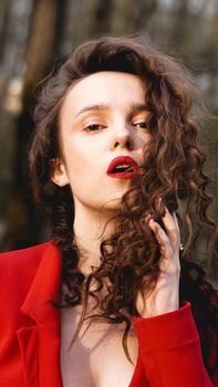 Glamorous woman wearing red outfit and matching red lip gloss. Portrait in the park