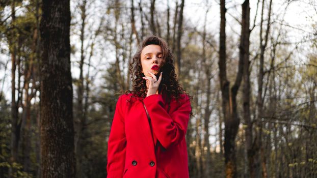 Glamorous woman wearing red outfit and matching red lip gloss. Portrait in the park