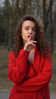 Glamorous woman wearing red outfit and matching red lip gloss. Portrait in the park