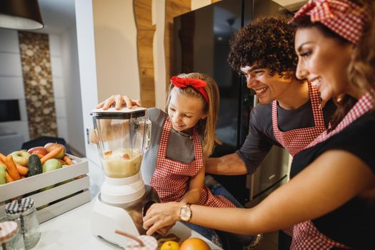 A cheerful parents and their young daughter trying a new recipe in the kitchen together.