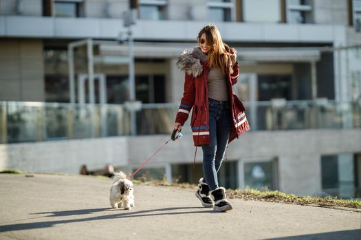 A smiling young woman walking with her cute Shih Tzu dog by the city street.