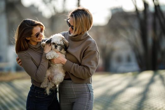 Portrait of a two young female friends with their pet Shih Tzu dog at the city.