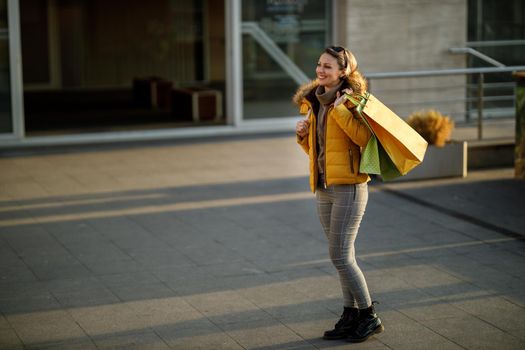 A pretty smiling mature woman walking outdoors in the street while holding shopping bags.