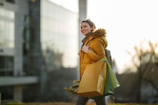 A pretty smiling mature woman walking outdoors in the street while holding shopping bags.