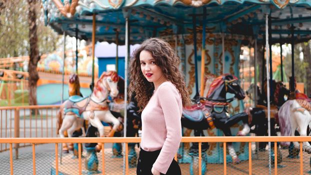 Stylish young hipster woman posing outdoors on the background of carousels. Girl enjoys a summer day