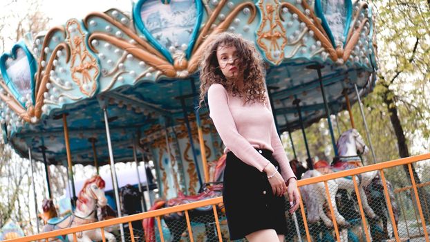 Stylish young hipster woman posing outdoors on the background of carousels. Girl enjoys a summer day