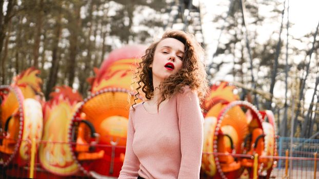 Stylish young hipster woman posing outdoors on the background of carousels. Girl enjoys a summer day