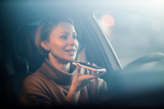 A beautiful mature woman talking voice message on a smart phone while driving her car.