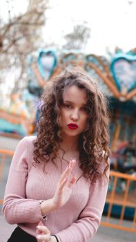 Stylish young hipster woman posing outdoors on the background of carousels. Girl enjoys a summer day