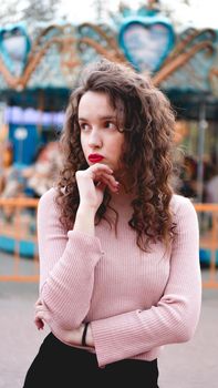 Stylish young hipster woman posing outdoors on the background of carousels. Girl enjoys a summer day