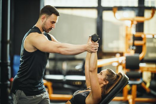 Shot of an attractive young woman working out with personal trainer at the gym.