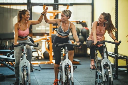 Group of three fit female friends having sports training on exercise bikes in a gym.