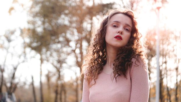 Closeup of a beautiful young woman with curly hair - a sunset behind her