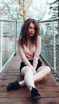 Fashion portrait of trendy young woman sitting near the netting rabitz in the city