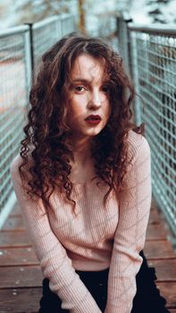 Fashion portrait of trendy young woman sitting near the netting rabitz in the city