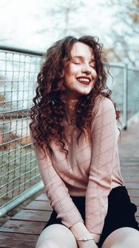 Fashion portrait of trendy happy young woman sitting near the netting rabitz in the city