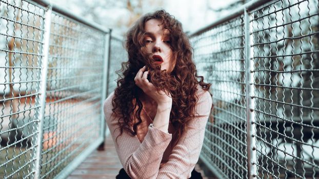 Fashion portrait of trendy young woman sitting near the netting rabitz in the city