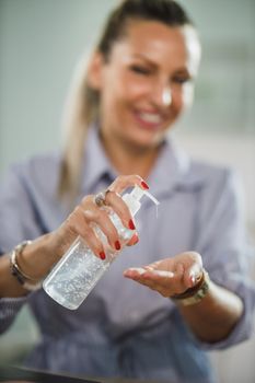 A smiling woman using antiseptic gel to disinfect her hands at her home office during corona virus pandemic.