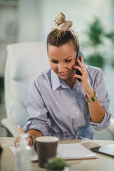 An attractive business woman sitting alone and talking on her cellphone during the day at home office.