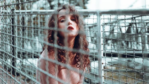 Fashion portrait of trendy young woman sitting near the netting rabitz in the city