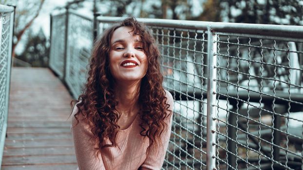 Fashion portrait of trendy happy young woman sitting near the netting rabitz in the city