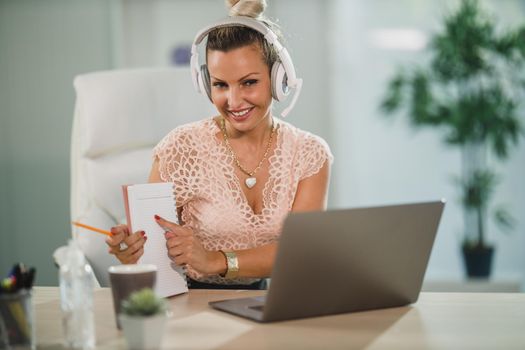 An attractive business woman with headphones working in a call center and talking with client online at her laptop.