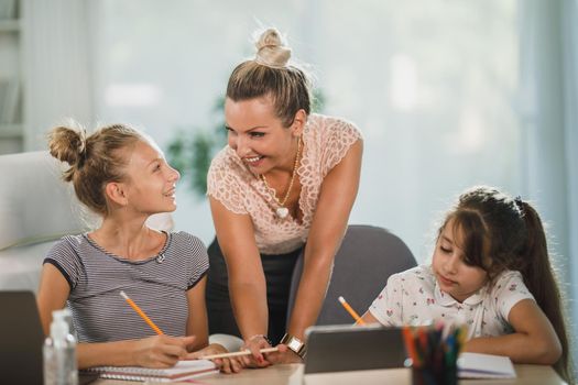 A beautiful single mother helping hers two daughters with homework at home.