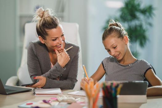 A beautiful single mother helping her cute teenage daughter with homework at home.
