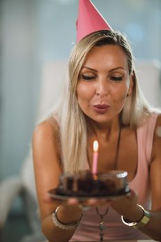 Portrait of a cheerful attractive woman holding a birthday cake and blowing candles.