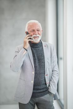 Portrait of a confident senior businessman talking on a smart phone while standing in a modern office.
