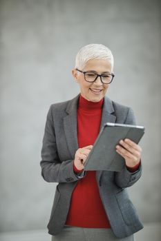 Portrait of a confident mature businesswoman working on a digital tablet while standing in a modern office.