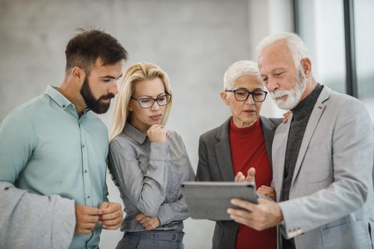 A group of confident business people using digital tablet  and having a discussion with each other during the meeting in a modern office.