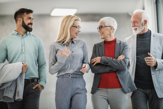 A group of smiling businesspeople walking and talking in a modern office.