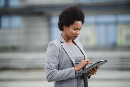 Portrait of a successful black business woman using digital tablet during quick break in front a corporate building.