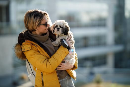 Portrait of an attractive woman bonding with her cute Shih Tzu dog outdoors.