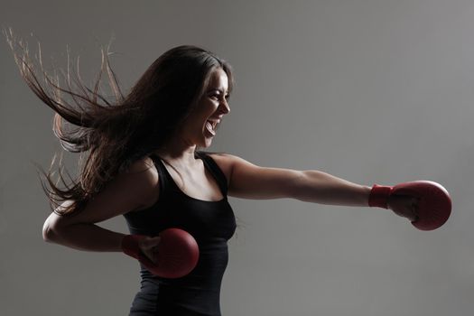 girl exercising karate punch and screaming against gray background