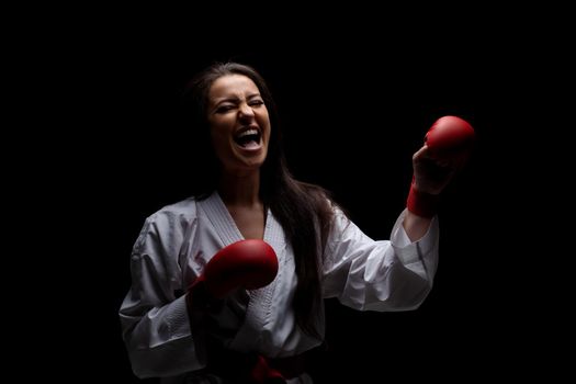 karate girl smiling in kimono and red gloves against black background