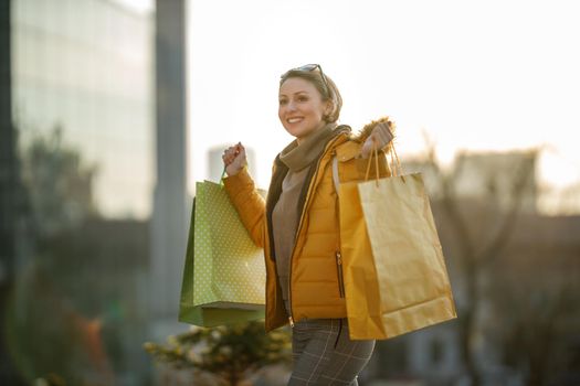 A pretty smiling mature woman walking outdoors in the street while holding shopping bags.